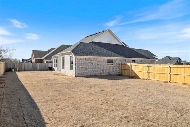 back of property with a fenced backyard, roof with shingles, central AC, and brick siding