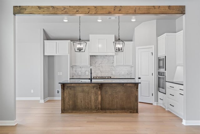 kitchen with light wood-style floors, beamed ceiling, dark countertops, and white cabinets