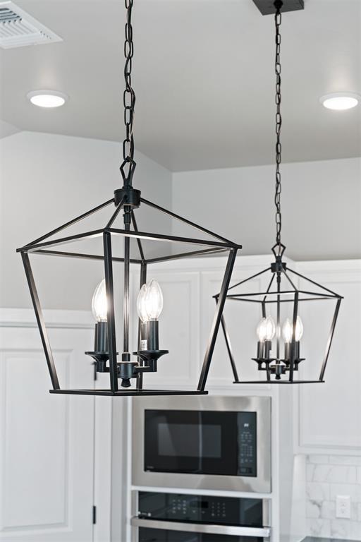 details featuring wall oven, visible vents, a chandelier, stainless steel microwave, and white cabinetry