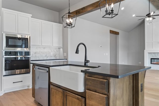 kitchen with stainless steel appliances, a sink, tasteful backsplash, dark countertops, and a glass covered fireplace