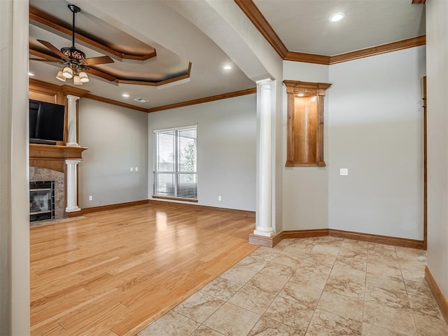 unfurnished living room featuring decorative columns, a raised ceiling, a ceiling fan, a fireplace with flush hearth, and wood finished floors