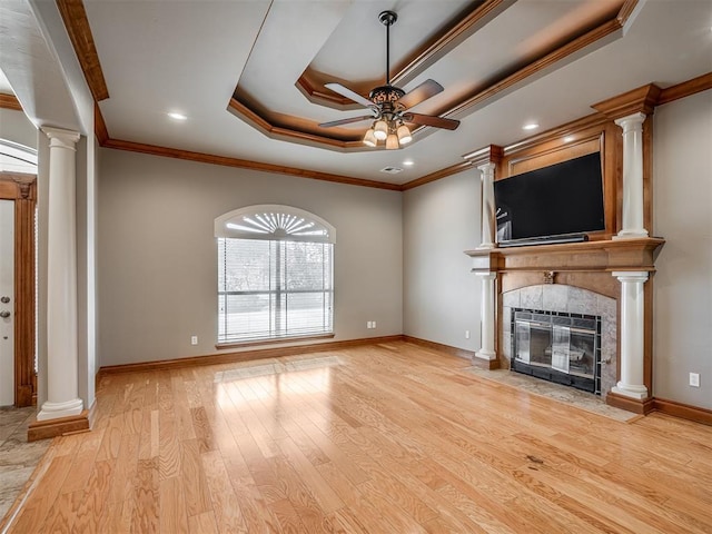 unfurnished living room with a tile fireplace, ceiling fan, decorative columns, a tray ceiling, and light hardwood / wood-style floors