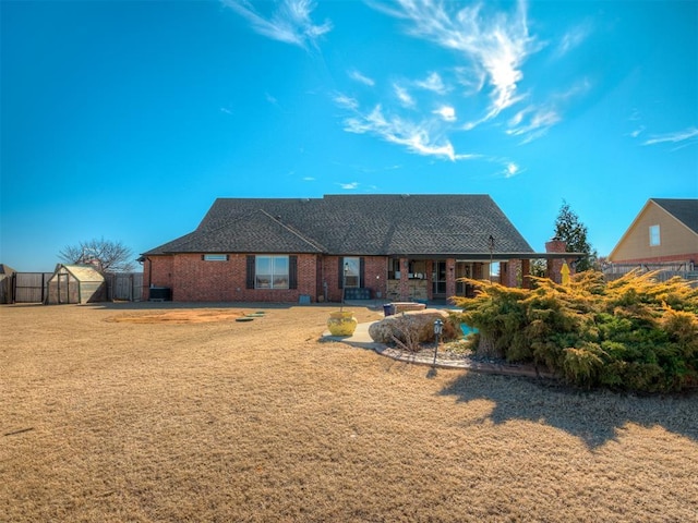 rear view of house featuring brick siding, a yard, an outdoor structure, and fence