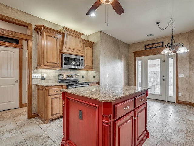 kitchen featuring light stone counters, hanging light fixtures, appliances with stainless steel finishes, a kitchen island, and backsplash