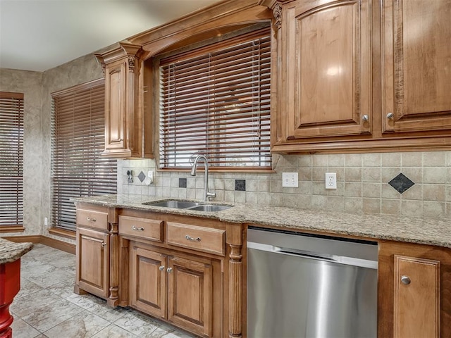 kitchen with stainless steel dishwasher, decorative backsplash, a sink, and light stone countertops