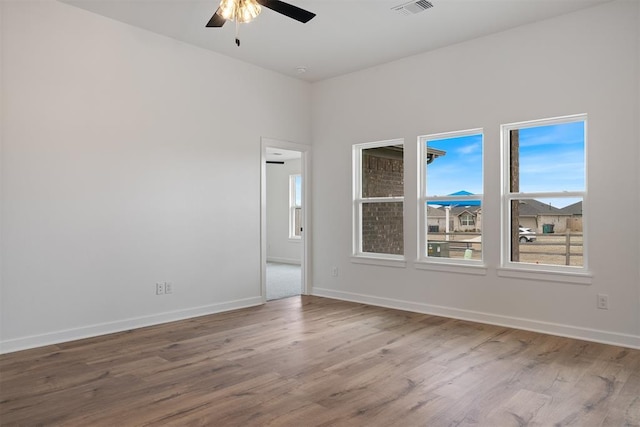 unfurnished room with wood finished floors, a ceiling fan, visible vents, and baseboards
