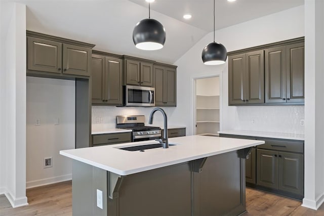 kitchen featuring light countertops, vaulted ceiling, appliances with stainless steel finishes, wood finished floors, and a sink