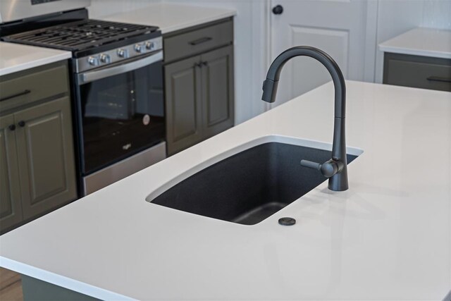 kitchen with stainless steel gas range oven, gray cabinets, light countertops, and a sink