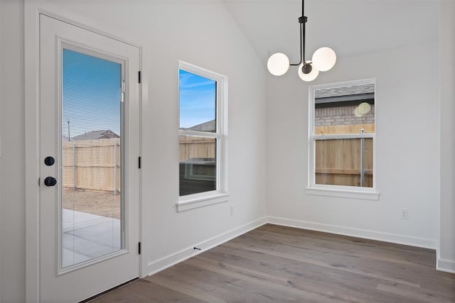 unfurnished dining area featuring an inviting chandelier, lofted ceiling, wood finished floors, and baseboards