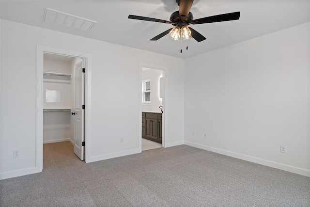 unfurnished bedroom with visible vents, a walk in closet, baseboards, light carpet, and a closet