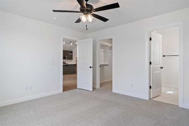 unfurnished bedroom with a walk in closet, light carpet, baseboards, and a closet