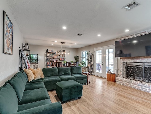 living room with french doors, a textured ceiling, light hardwood / wood-style floors, and a fireplace