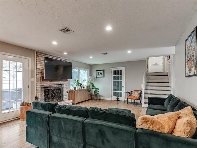 living room with a brick fireplace, a textured ceiling, and light wood-type flooring