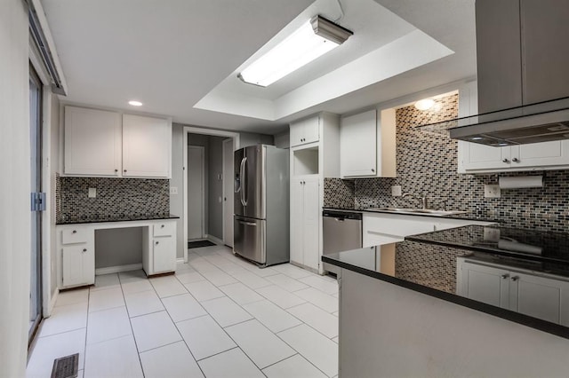 kitchen featuring white cabinetry, appliances with stainless steel finishes, a tray ceiling, island exhaust hood, and decorative backsplash