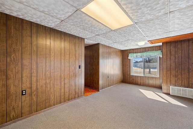 carpeted empty room featuring a paneled ceiling and wood walls