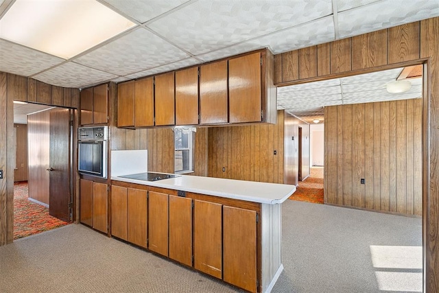 kitchen with wall oven, wooden walls, black electric cooktop, and light carpet