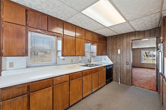 kitchen with sink, a paneled ceiling, dishwasher, light carpet, and wood walls