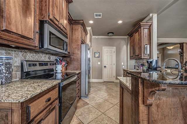 kitchen featuring light tile patterned floors, appliances with stainless steel finishes, dark stone countertops, a kitchen breakfast bar, and ornamental molding