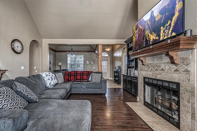 living area with arched walkways, a tiled fireplace, dark wood finished floors, and lofted ceiling