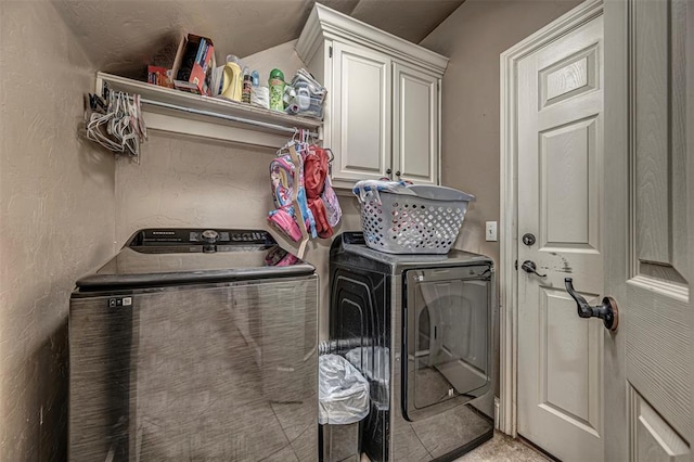 laundry area featuring cabinet space, a textured wall, and washer and clothes dryer