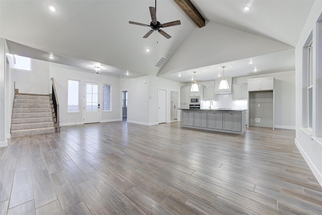 unfurnished living room with beamed ceiling, ceiling fan, high vaulted ceiling, and light hardwood / wood-style floors