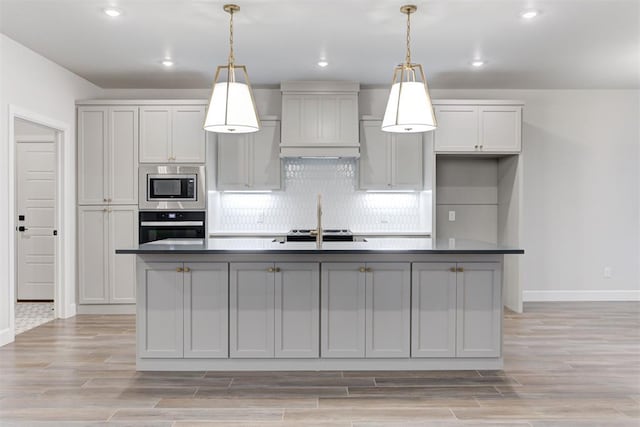 kitchen featuring custom exhaust hood, an island with sink, appliances with stainless steel finishes, and gray cabinetry