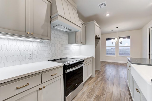 kitchen featuring tasteful backsplash, stainless steel electric range oven, decorative light fixtures, light wood-type flooring, and custom range hood