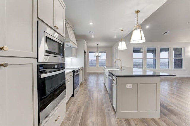 kitchen featuring appliances with stainless steel finishes, pendant lighting, sink, white cabinets, and a kitchen island with sink