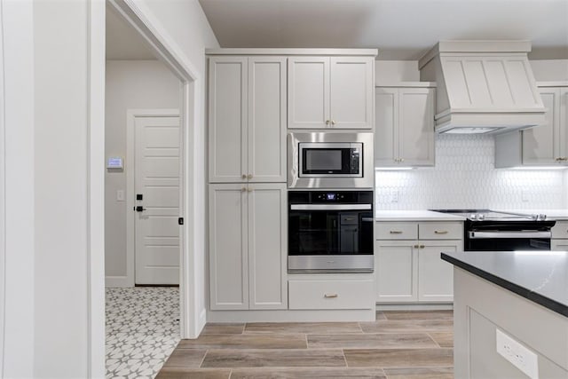 kitchen with backsplash, stainless steel appliances, white cabinets, and premium range hood