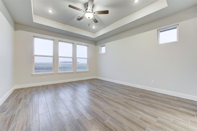 empty room with a tray ceiling, light hardwood / wood-style flooring, and ceiling fan