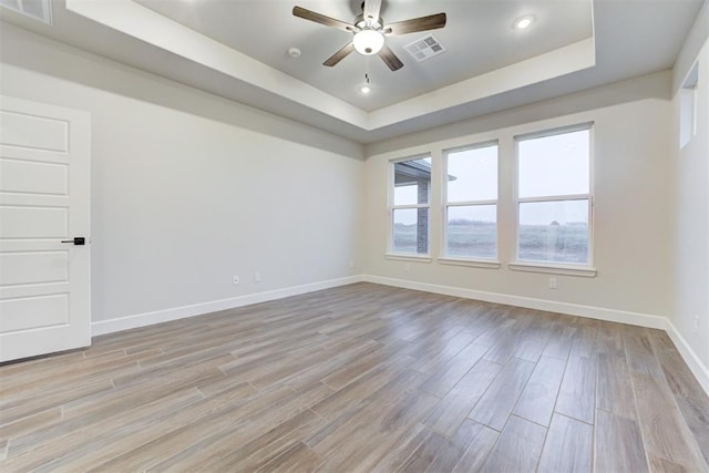 empty room featuring a raised ceiling, ceiling fan, and light hardwood / wood-style flooring