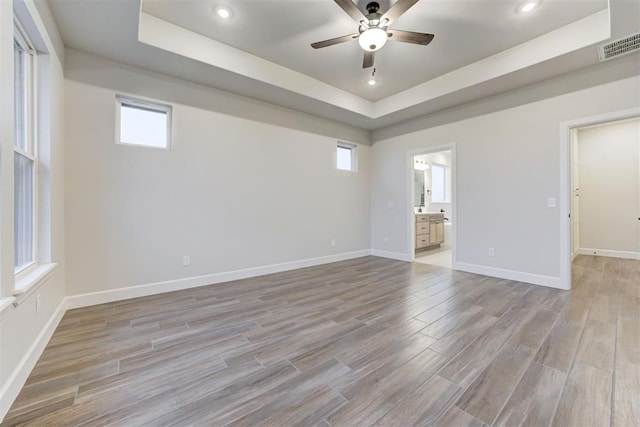 empty room featuring ceiling fan, a tray ceiling, and light hardwood / wood-style flooring