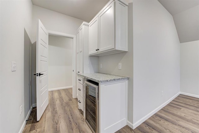 kitchen featuring light stone countertops, wine cooler, white cabinets, and light hardwood / wood-style flooring