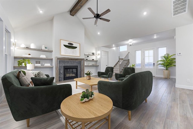 living room featuring beam ceiling, high vaulted ceiling, ceiling fan, a fireplace, and light hardwood / wood-style floors