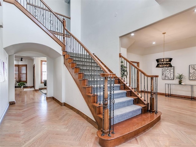 stairs featuring parquet floors, a chandelier, and a high ceiling