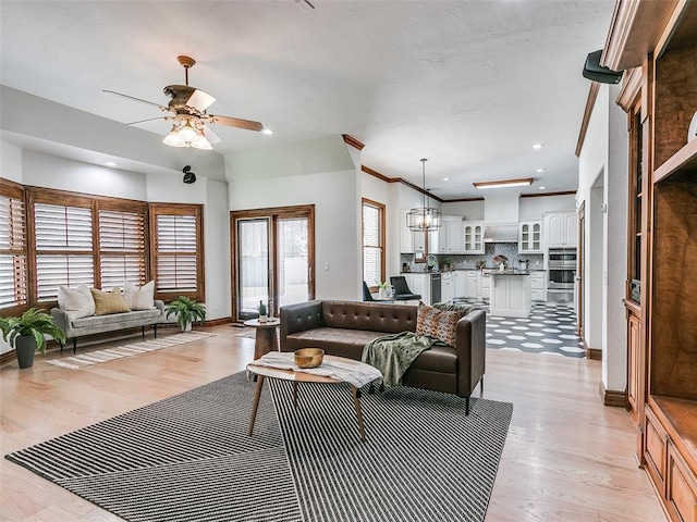 living room featuring crown molding, ceiling fan with notable chandelier, and light hardwood / wood-style floors