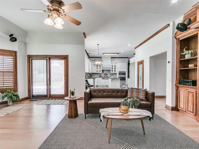 living room featuring ceiling fan with notable chandelier, ornamental molding, and light wood-type flooring