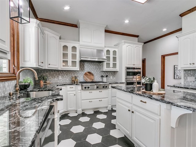 kitchen with pendant lighting, wall chimney range hood, sink, appliances with stainless steel finishes, and white cabinetry