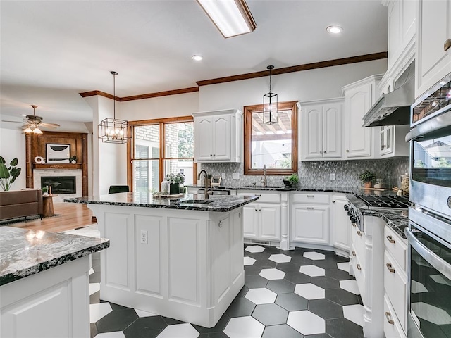 kitchen with white cabinetry, decorative light fixtures, a center island with sink, and dark stone countertops