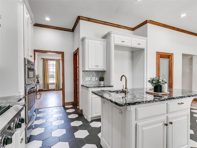 kitchen featuring dark stone counters, sink, a center island with sink, and white cabinets