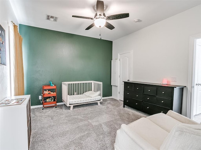 carpeted bedroom with a crib and ceiling fan