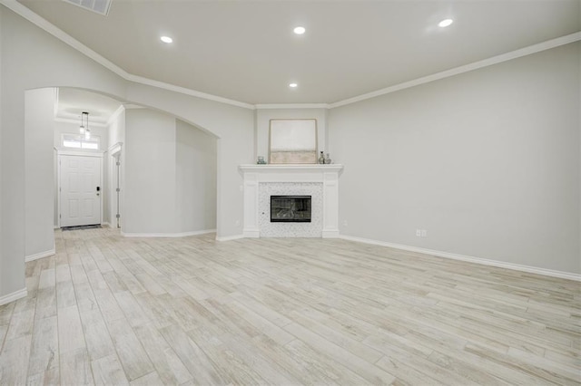 unfurnished living room featuring a tiled fireplace, ornamental molding, and light hardwood / wood-style floors