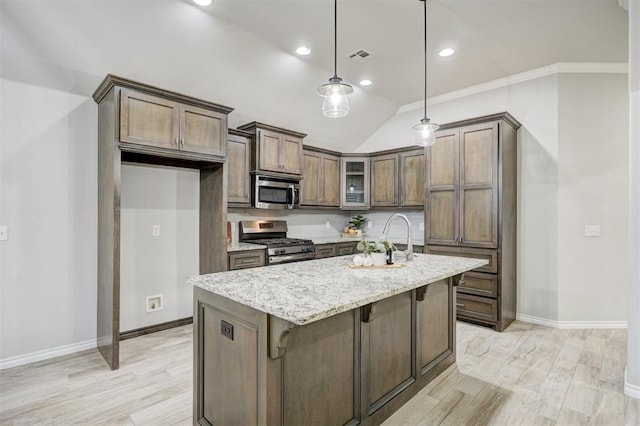 kitchen featuring appliances with stainless steel finishes, an island with sink, sink, hanging light fixtures, and light stone countertops