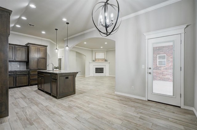 kitchen featuring pendant lighting, dark brown cabinets, a center island with sink, decorative backsplash, and stainless steel dishwasher