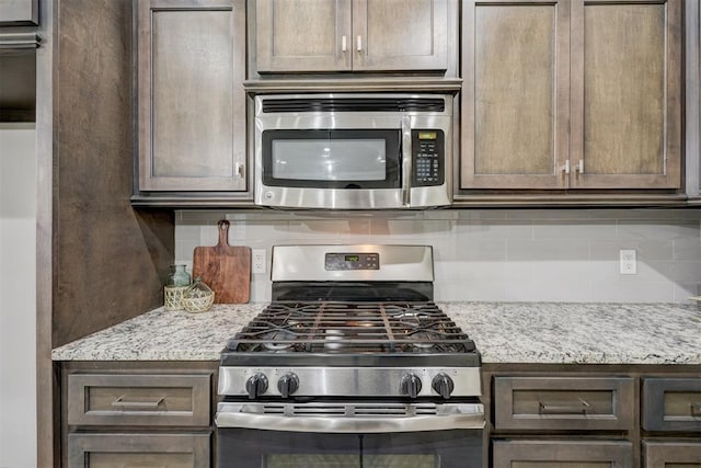 kitchen with stainless steel appliances, light stone countertops, dark brown cabinets, and decorative backsplash