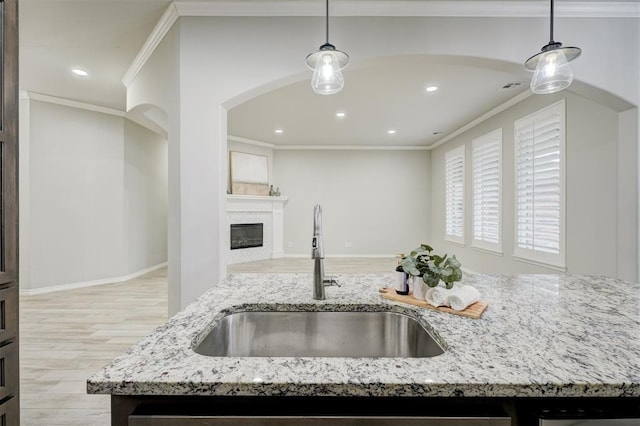 kitchen featuring pendant lighting, sink, light stone counters, and a center island with sink