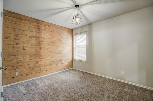 carpeted spare room with a notable chandelier and wood walls