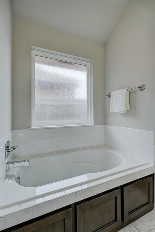 bathroom with a healthy amount of sunlight, tiled bath, and vaulted ceiling