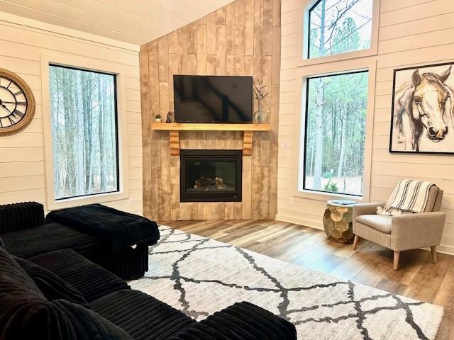 living room with wood walls, lofted ceiling, a fireplace, and light wood-type flooring