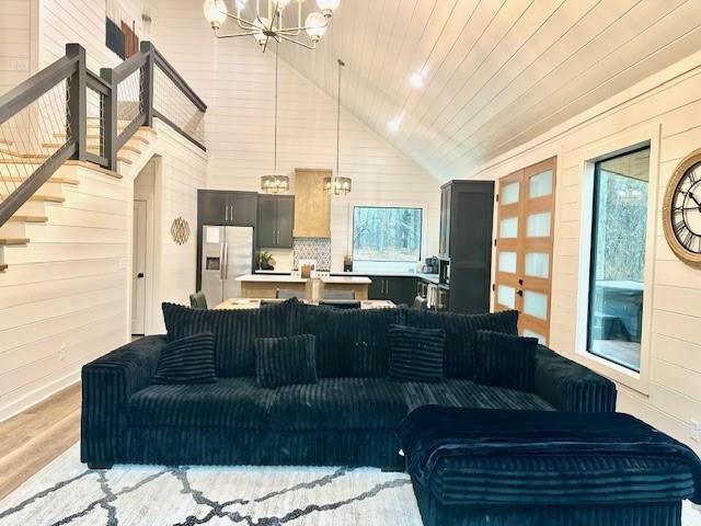 living room with wooden walls, high vaulted ceiling, light hardwood / wood-style floors, wooden ceiling, and a chandelier